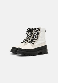White and black ankle boots with a textured upper, lace-up design, and thick black rubber sole. Features padded collar and contrasting accents.