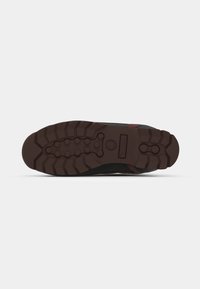Black shoe sole with a brown textured rubber tread. Features a central logo and a rugged design, suitable for outdoor use.