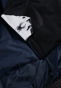 Mehrfarbiger Stoff mit einem schwarzen Mesh-Panel, einem navyblauen Nylon-Basis und einer weißen Grafik mit einer schwarzen Illustration. Weich und strukturiert.