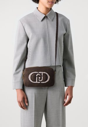 Brązowa torebka z miękkim, haftowanym logo, o prostokątnym kształcie, zamykana na zamek błyskawiczny, z długim paskiem, w zestawie z ubraniem w kratę.