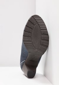 Semelle d'une botte bleu foncé avec une semelle texturée et un talon empilé, positionnée sur un fond blanc en coin.