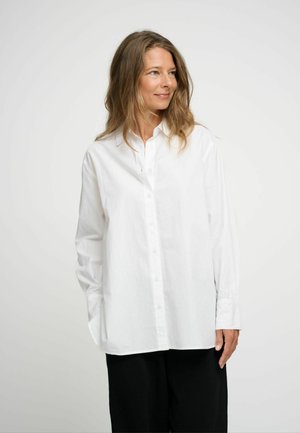 Camicia bianca con bottoni, maniche lunghe, realizzata in cotone. Presenta un colletto classico e una vestibilità ampia, abbinata a pantaloni neri.