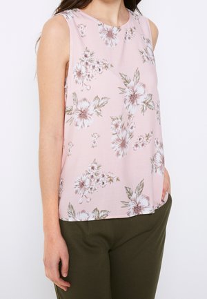 Haut sans manches en tissu rose pâle avec un imprimé floral blanc et vert. Encolure ronde et coupe décontractée, associé à un pantalon vert olive.