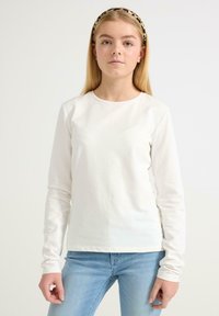 Langærmet hvid bomulds skjorte med rund halsudskæring, parret med lyseblå jeans. Stoffet er glat og let.