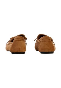 Paire de mocassins en daim marron avec pompons, vus de dos sur un fond blanc.