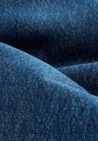 Gros plan d'un tissu en denim bleu plié montrant la texture détaillée du tissage et des nuances variées d'indigo.