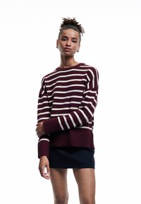 Bordeauxrood en witte gestreepte gebreide trui met geribde manchetten en onderrand. Relaxte pasvorm, ronde halslijn, gedragen over een donkere rok.