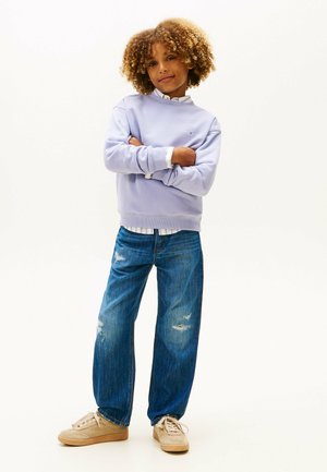 Sudadera de lavanda claro con puños acanalados, combinada con jeans azules desgastados. Zapatillas en tonos neutros completan el look casual.