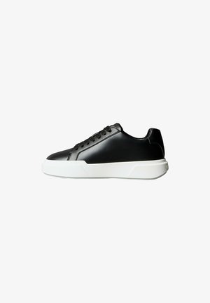 Schwarzer niedriger Schnürsneaker mit glattem Lederobermaterial und dicker weißer Gummisohle, Seitenansicht vor weißem Hintergrund.