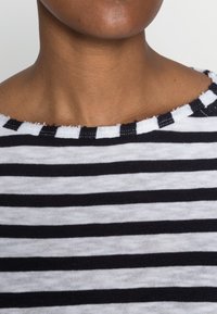 Haut à rayures noires et blanches avec un col large et effiloché. Le tissu semble doux, avec des rayures alternant entre épaisses et fines.