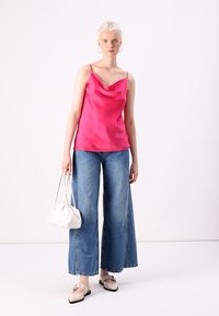 Lyserød satin top med draperet hals, parret med brede blå denim jeans. Tilbehøret inkluderer en hvid håndtaske og beige slip-on sko.