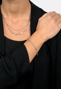 Silver layered necklaces with decorative charms and a matching bracelet. Smooth metal texture, geometric links, and minimalist design.