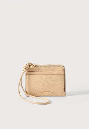 Béžový kožený držiak na karty s náramkom, zlatý zips MK a logo Michael Kors na prednej strane na jednoliatom pozadí.