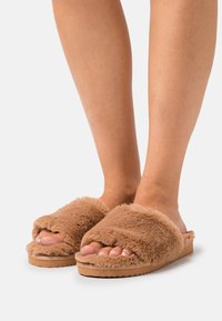 Brown faux fur slide slippers with a soft texture, wide top straps, and a flat rubber sole, designed for comfort and casual wear.