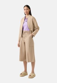 Beige cropped jakke og vidde bukser, parret med en lilla ribbet top og lyse platform sandaler. Stoffet ser blødt og glat ud.