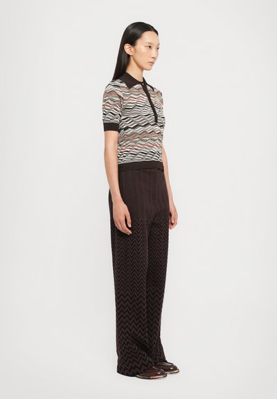 Knit polo shirt in multicolored wave pattern, short sleeves, and dark collar, paired with wide brown zigzag-pattern trousers and brown shoes.