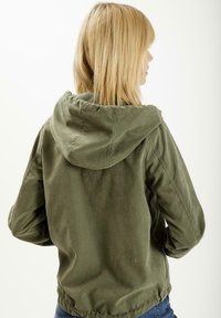 Oliwkowa kurtka z kapturem, wykonana z gładkiego materiału, z ściągniętym w pasie i elastycznymi mankietami. Posiada luźny krój i prosty design.