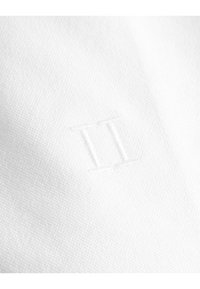 Tessuto bianco con una sottile texture caratterizzato da un dettaglio in rilievo "II". Il design è minimalista e si concentra sulla semplicità.