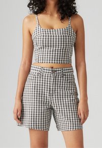 Ensemble crop top et short à carreaux marron, blanc et noir. Tissu en coton avec un design ajusté, présentant une encolure carrée et une taille à boutons.