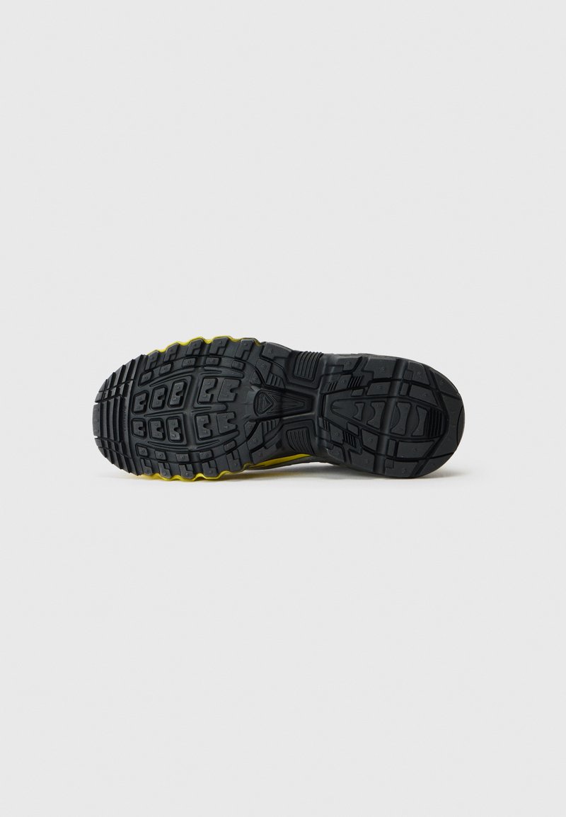 Sort og gul sneaker sål med dybe dækmønstre designet til greb, vist fladt mod en enkel hvid baggrund.
