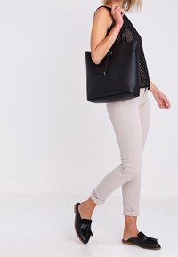 Czarna torba tote z gładkiego materiału syntetycznego, przestronnym wnętrzem, minimalistycznym kształtem i regulowanym zamknięciem na sznurek.