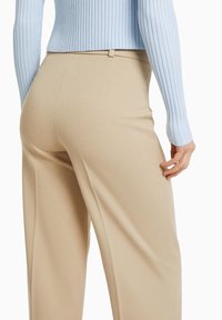 Celana panjang lebar berwarna beige dengan tekstur halus dan lipatan halus. Dipadukan dengan atasan lengan panjang berwarna biru muda dengan model ribbed yang memiliki manset pas.