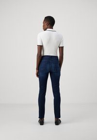 Geribbeld wit poloshirt met zwarte afwerking, gecombineerd met donkerblauwe slim fit jeans met achterzakken. Model draagt zwarte schoenen.