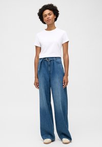 Spodnie dżinsowe o szerokich nogawkach w kolorze niebieskim z wysokim stanem, z paskiem z złotym zapięciem, w połączeniu z białą koszulką z okrągłym dekoltem.