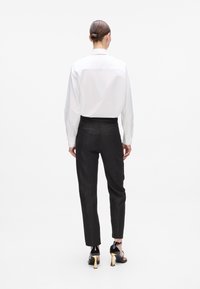 White long-sleeve shirt with a classic collar, paired with black textured tapered pants. Silver and black open-toe high heels accentuate the look.