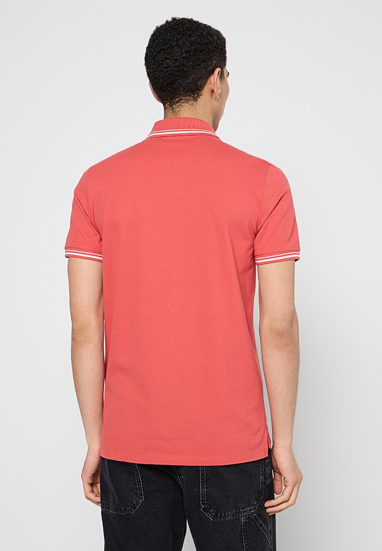 Koralo polo z krótkim rękawem z białymi paskami na kołnierzyku i mankietach, wykonany z miękkiej, gładkiej bawełny.