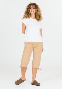 Valkoinen puuvillapaita, vaaleat lyhyet housut, joissa on nauhat nilkoissa, ja ruskeat liukuKlomikengät. Yksinkertainen, rento istuvuus.