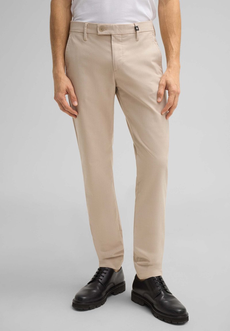 Beige Hose mit glatter Textur, geradem Schnitt und vorderen Taschen. Kombiniert mit schwarzen Schnürschuhen für einen eleganten Look.