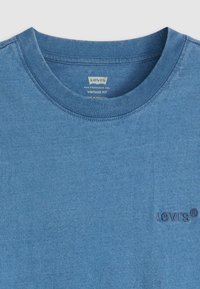Blå bomull T-skjorte med rund hals, med et brodert Levi's-logo på venstre bryst. Glatt tekstur med svake fargevariasjoner.