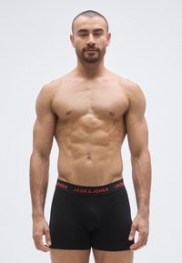 Boxers noirs avec une ceinture rouge portant le texte « JACK & JONES ». Tissu lisse, coupe ajustée, mettant en valeur les contours du corps.