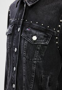 Mustat farkkutakki, jossa on hopeiset niitit harteilla, kaksi rintataskua ja napitus. Takissa on brändilogo kankaassa.