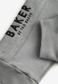 Sivá mikina so vzorovanými manžetami a embosovaným logom "BAKER by Ted Baker" v čiernej farbe na boku. Hladká textúra s neformálnym dizajnom.