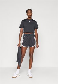 Čierny crop top a čierne šortky, oboje s bielymi olemovaniami. Šortky majú elastický pás a vrecká. Biele tenisky a čierny doplnok.