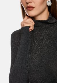 Dunkelgrauer Rollkragenpullover aus einem glitzernden, strukturierten Material. Verfügt über lange Ärmel und ein tailliertes Design. Ein dezenter Glanz betont den Stoff.