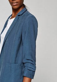 Blauer, leichter Blazer mit glatter Textur, einer einzelnen Vorderentasche und hochgekrempelten Ärmeln, ausgestattet mit einem klassischen Kragen.