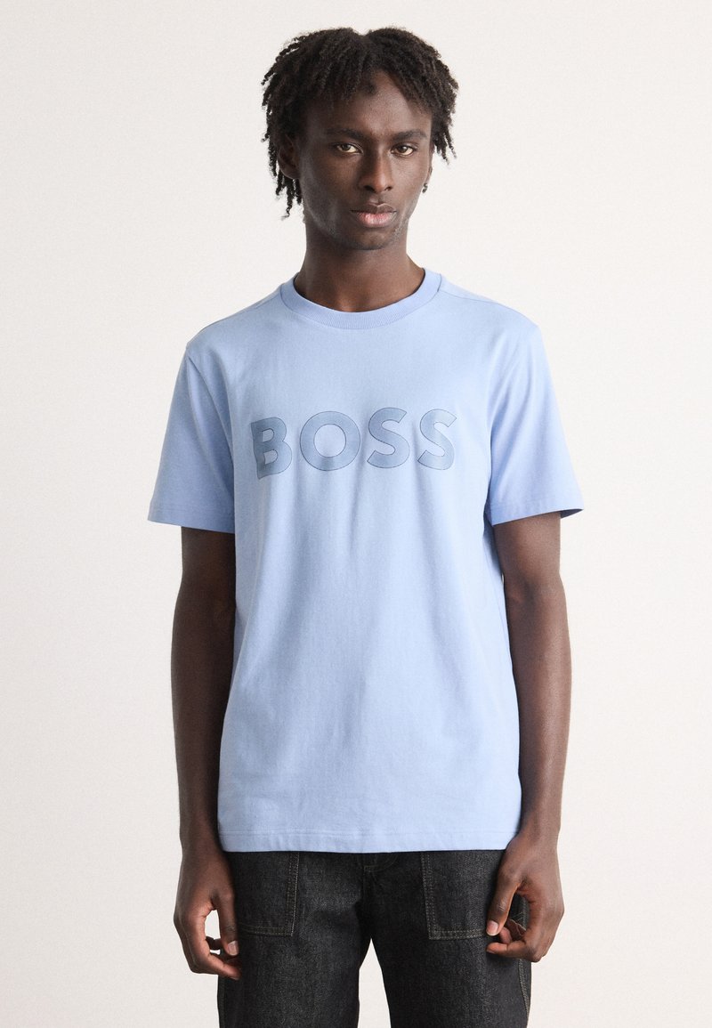 Světle modré bavlněné tričko s krátkým rukávem, které má výrazné, texturované logo "BOSS" v tmavším odstínu. Kulatý výstřih, volný střih.