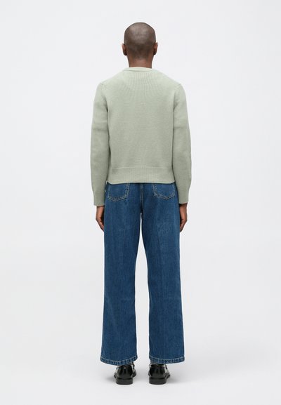 Suéter de punto verde claro con dobladillo acanalado, combinado con jeans de mezclilla azul holgados y zapatos negros. Vista trasera, sin patrones ni logotipos visibles.