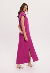 Fuksjowa maxi sukienka z kołnierzykiem, krótkimi podwiniętymi rękawami i bocznym rozcięciem. Gładki materiał, prosty design, połączona ze srebrnymi sandałami na obcasie.