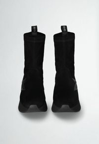 Stivaletti neri in suede con una texture morbida, caratterizzati da una punta arrotondata e una suola in gomma. Le linguette per il tallone si trovano sul retro.