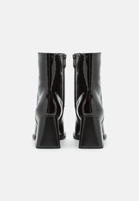 Botas de tobillo de charol negro con punta cuadrada y tacones gruesos. Presenta una cremallera en el lateral y un acabado liso y brillante.
