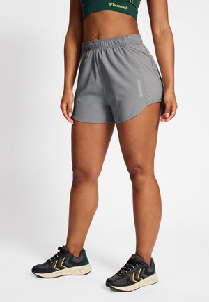 Grå atletiske shorts med en buet kant, elastisk talje og logo-detalje, sammen med sorte og grønne strukturerede løbesko.
