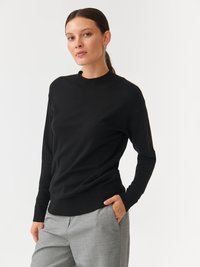 Fekete, könnyű pulóver kerek nyakú és bordás mandzsettával, szürke, texturált nadrággal párosítva. Az anyaga puhanak tűnik.