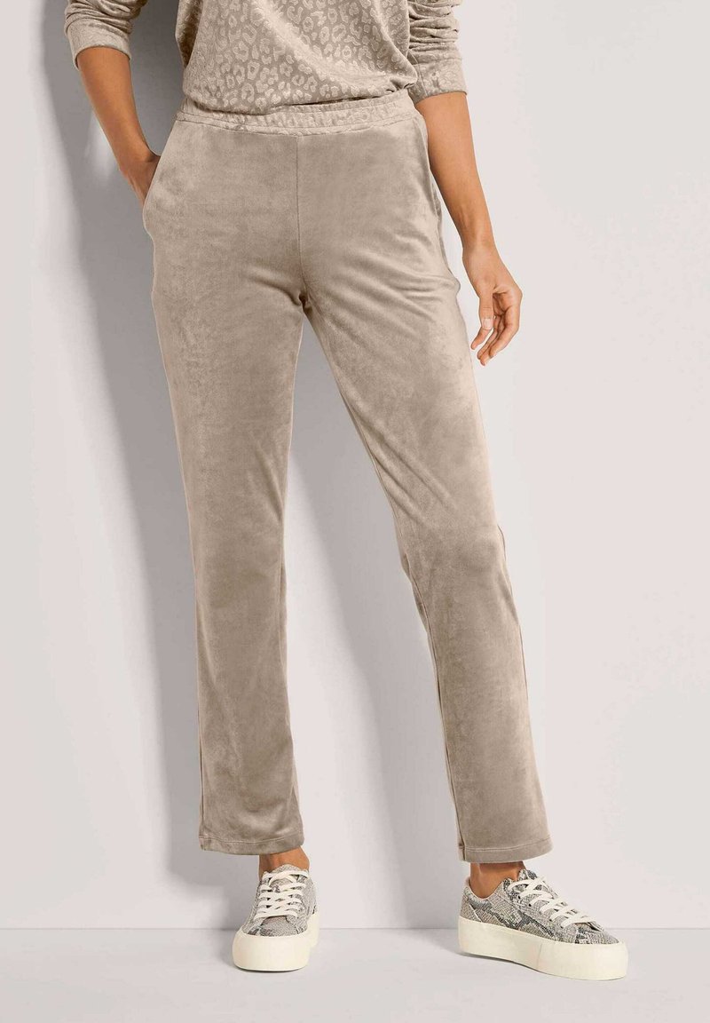 Beige velours joggers met een ontspannen pasvorm, voorzien van een elastische tailleband. Gecombineerd met grijze sneakers met slangenprint en een gedessineerde top.