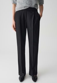 Pantalons noirs ajustés avec une texture lisse, un design à jambes larges et une taille élastique. Dotés de poches latérales et de plis avant nets.