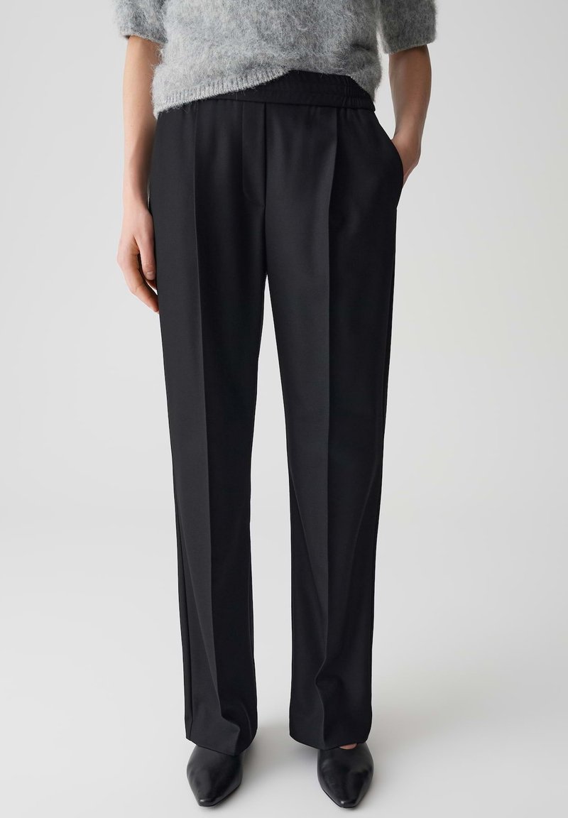 Pantalons noirs ajustés avec une texture lisse, un design à jambes larges et une taille élastique. Dotés de poches latérales et de plis avant nets.