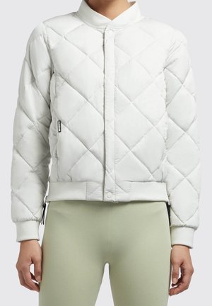 White quilted bomber jacket with ribbed collar, cuffs, and hem worn over light green textured pants, hands relaxed at sides.